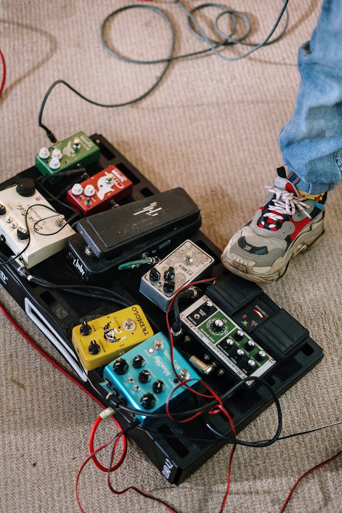 gallery-05 Close-up of a musician's foot on a pedalboard with various colorful guitar effects pedals in a home studio.